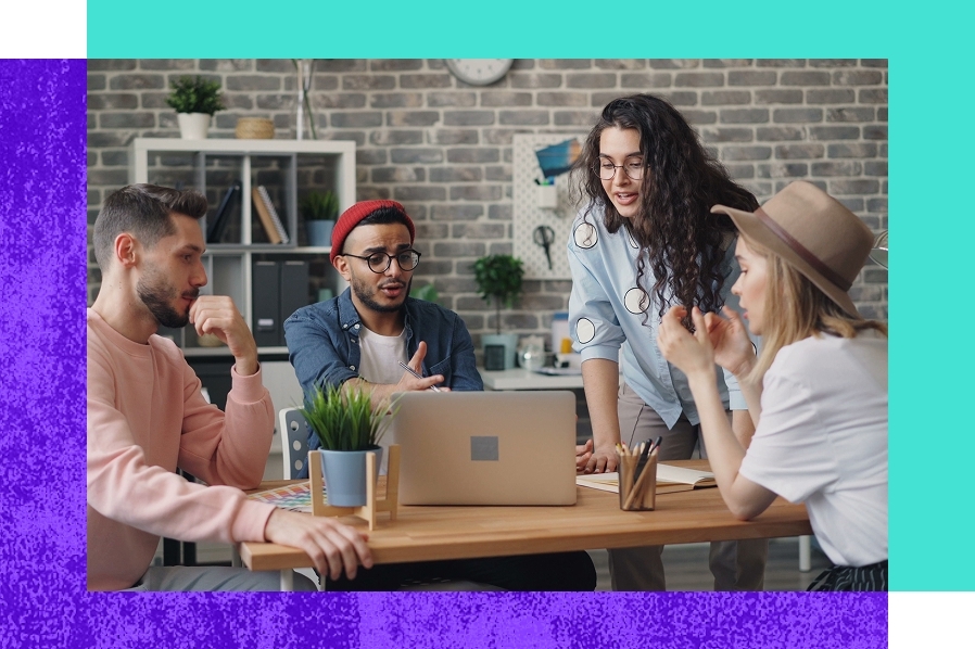 Team members collaborate in a creative workspace, sharing ideas and reviewing information around a laptop during a group discussion